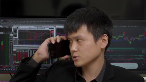 chinese businessman talking on the phone with stock market on computer monitors in background