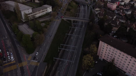 Aerial-tilt-up-above-a-railway-and-buildings-in-Lausanne,-Switzerland-at-dusk