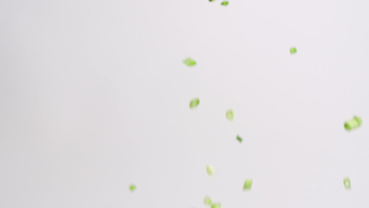 깍둑썰기하고 잘게 썬 녹색 양파 조각이 흰색 배경에 슬로우 모션으로 비가 내리고 있습니다.