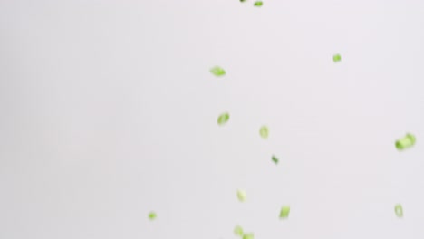 diced and chopped green onion pieces raining down on white backdrop in slow motion