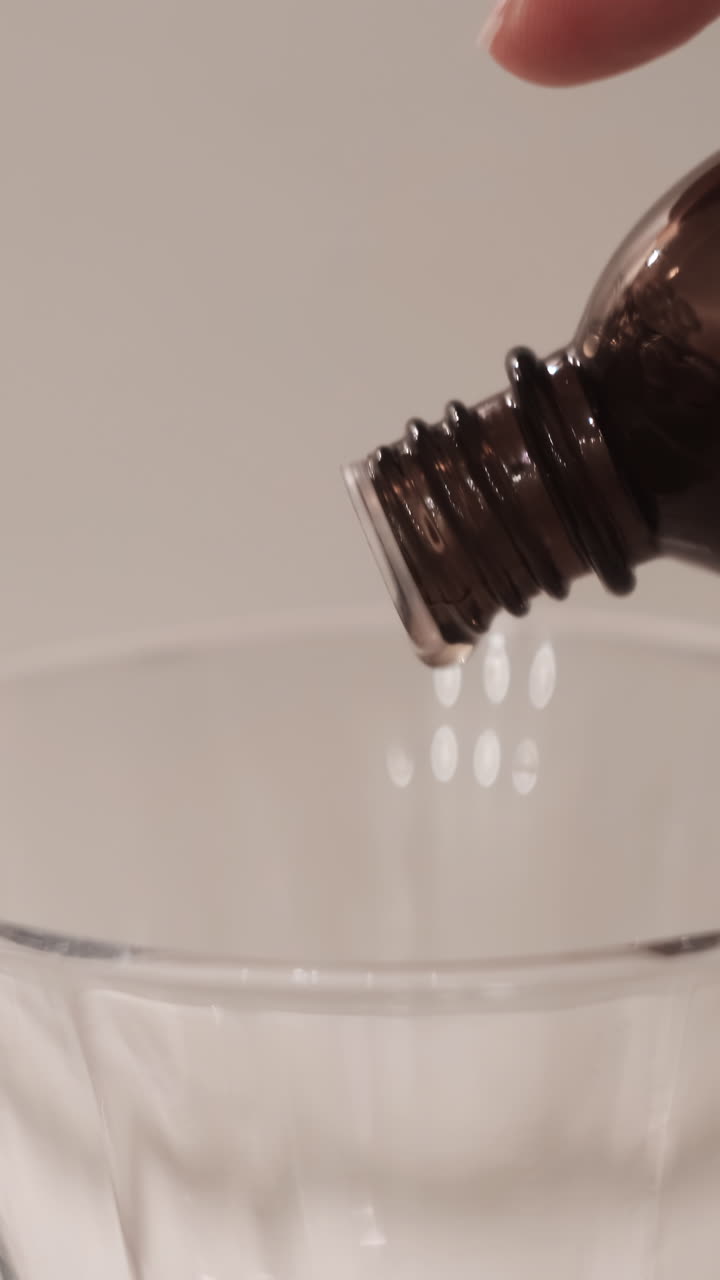 Versamento di liquido da bottiglia marrone scuro in contenitore di vetro
