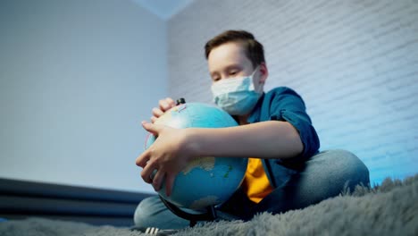 boy looking at globe. teenage boy wearing medical mask. concept of covid-19 pandemic infection.