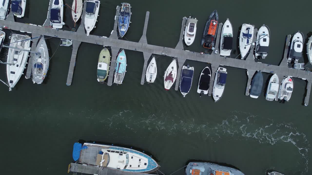 Top down aerial drone view above luxury moored private marina sailing ships and yacht boats following wake