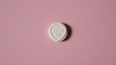 mano recogiendo caramelos de corazón con mensaje de niño de ensueño sobre fondo rosa