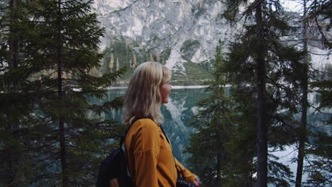 a blond haired girl walks along the shore of the lake braies laughing, dolomites