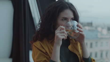 cheerful woman drinking tea and looking through window in office