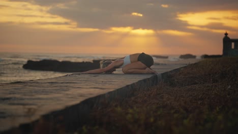 woman lowering head to ground during yoga child pose with golden sunset