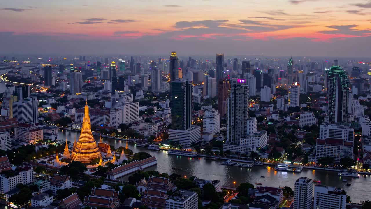 Aerial view of a cityscape at sunset, highlighting a lit temple and river