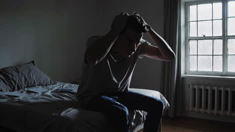 man sitting in a bedroom, appearing distressed.