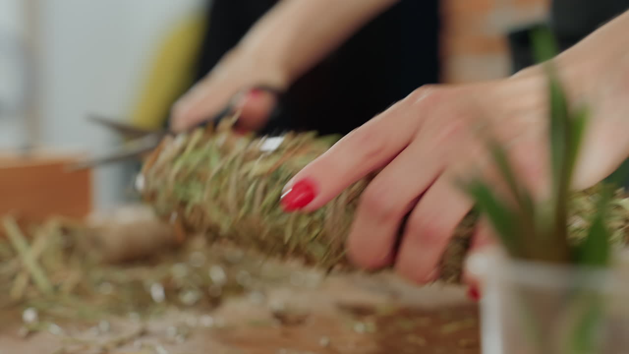 Closeup of woman holding handmade straw wreath during crafting process, rustic natural decoration prepared with dried grass and twine, for arrangement indoors