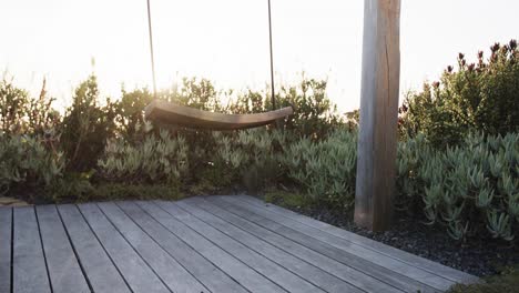 Swing-on-over-decking-in-tranquil-garden-at-sundown,-slow-motion