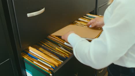 mujer abriendo un cajón negro lleno de archivos y carpetas y archivando algunos documentos