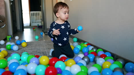 baby boy sitting on the floor among the balls and pulling one to his mouth. lovely child rushes ahead to fetch something.