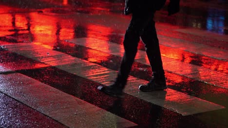 red streetlights reflect off wet road as person walks in crosswalk