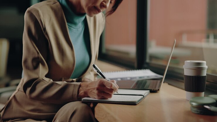 Donna che scrive su un quaderno con un portatile