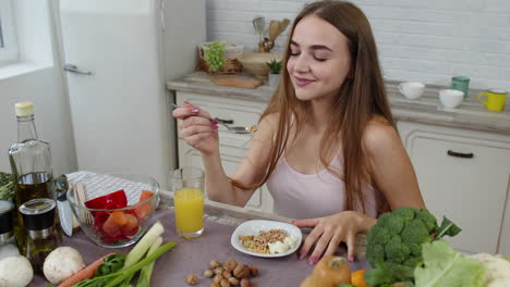 una chica encantadora comiendo brotes crudos de trigo sarraceno con nueces en la cocina con verduras y frutas frescas