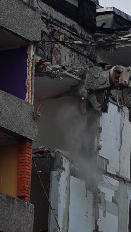 hydraulic claw of excavator breaks easily the floors of an old building. falling debris create thick dust cloud at the deconstruction site. vertical video