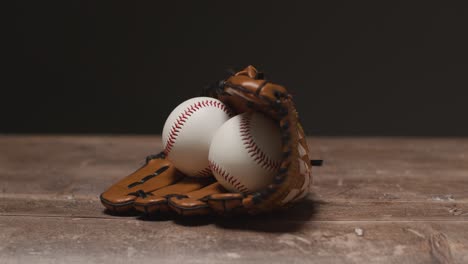 studio baseball shot with ball in catchers mitt and person picking up wooden bat from wooden background 1