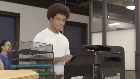 african american man at a printer in a busy office with video dolly left to right