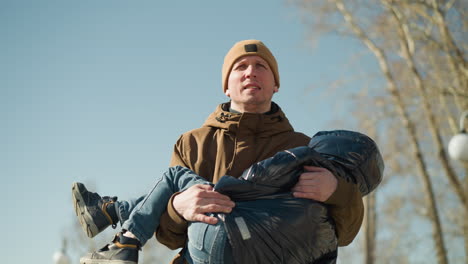 father carrying his child while walking down a path, appearing tired with his teeth been seen and blur view of trees and a light pole in view