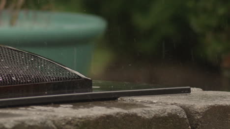 Heavy-rain-drops-falling-and-splashing-on-stone-firepit,-Slow-Motion