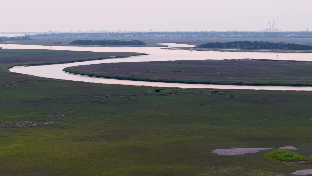 Drone footage captures a meandering river cutting through vast green marshland near Charleston, South Carolina, showcasing lush vegetation and tranquil waters from an aerial perspective