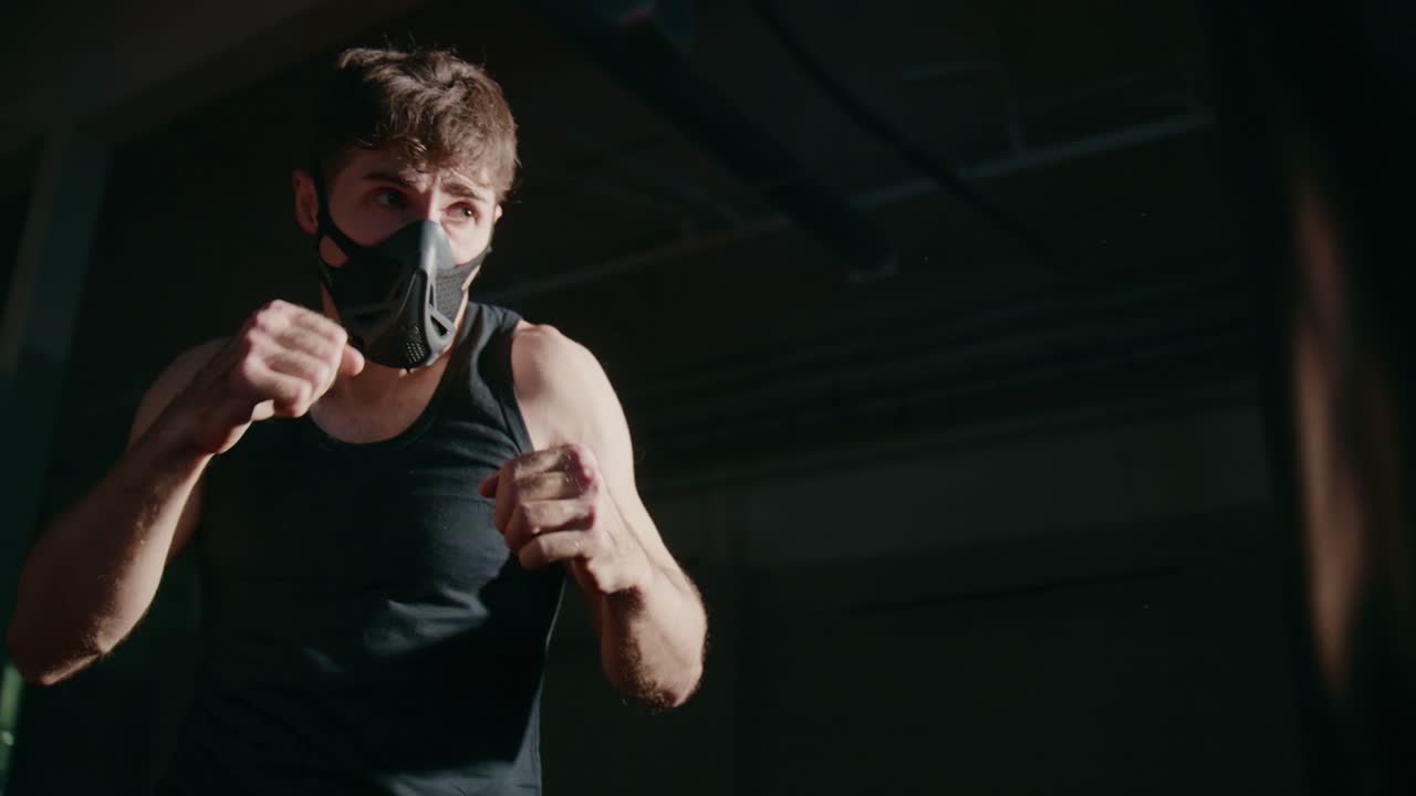 Young Man in Training Mask Punching in a Dark Gym