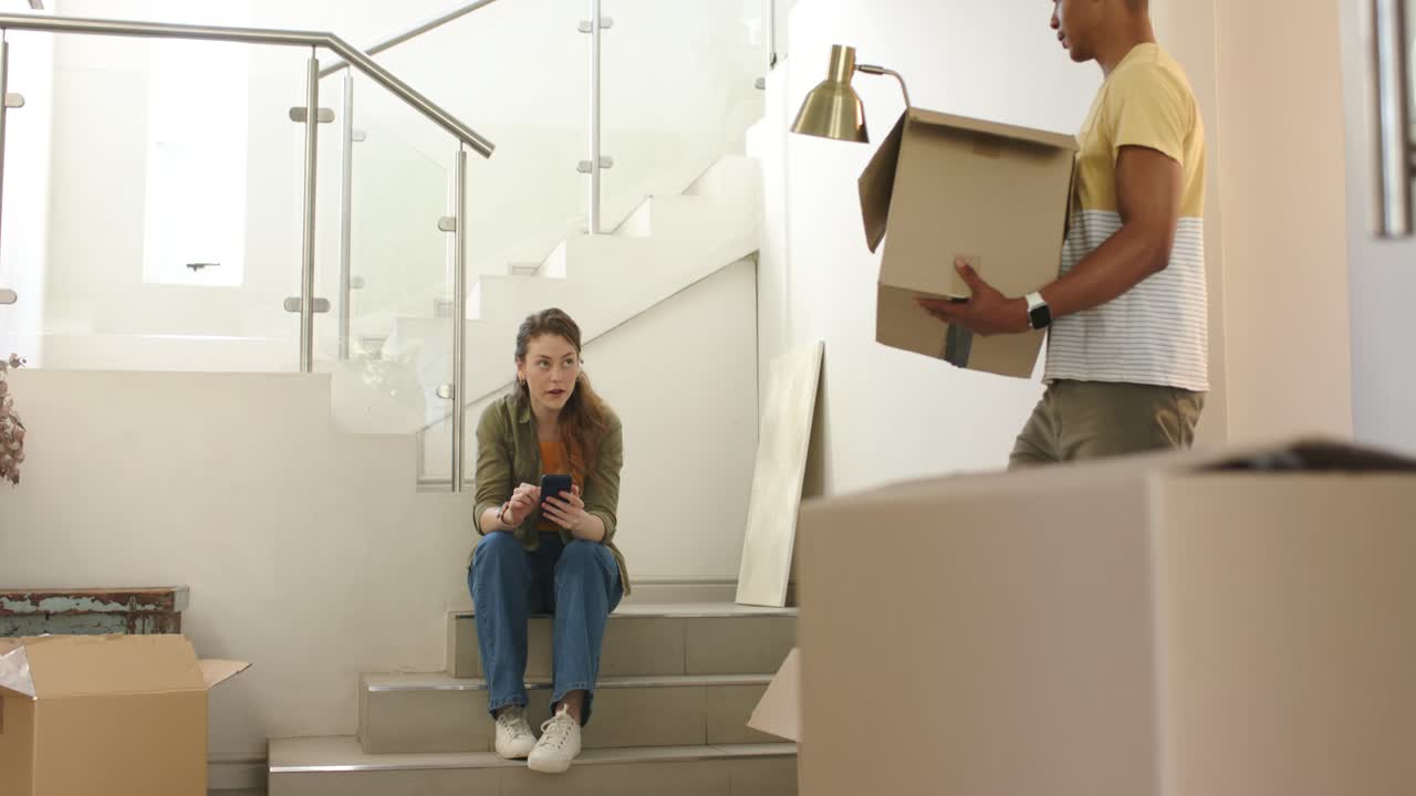Couple unpacking foyer boxes man entering with lamp making woman on step using phone looking up