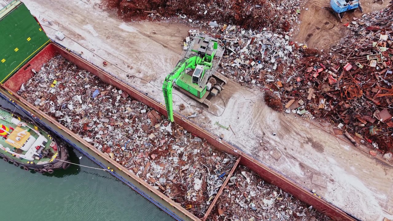 Operazione di riciclaggio in un deposito di rottami metallici vicino a un corso d'acqua di giorno