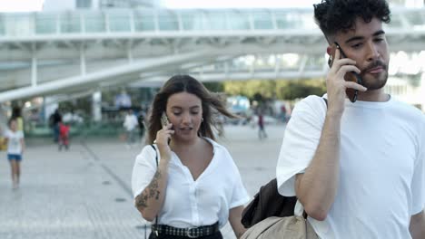 vista frontal de dos personas caminando por la calle con teléfonos inteligentes