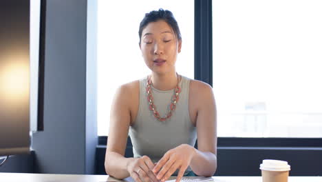 Portrait-of-asian-businesswoman-on-video-call-talking-to-camera-in-office,-slow-motion,-copy-space