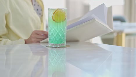 a woman siting on a table in the living room with her book and drink, close up shot, push in shot, pull out shot