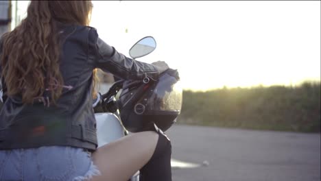 back view of a female biker with long hair sitting on the motorcycle seat. close up of young curly woman on the chopper