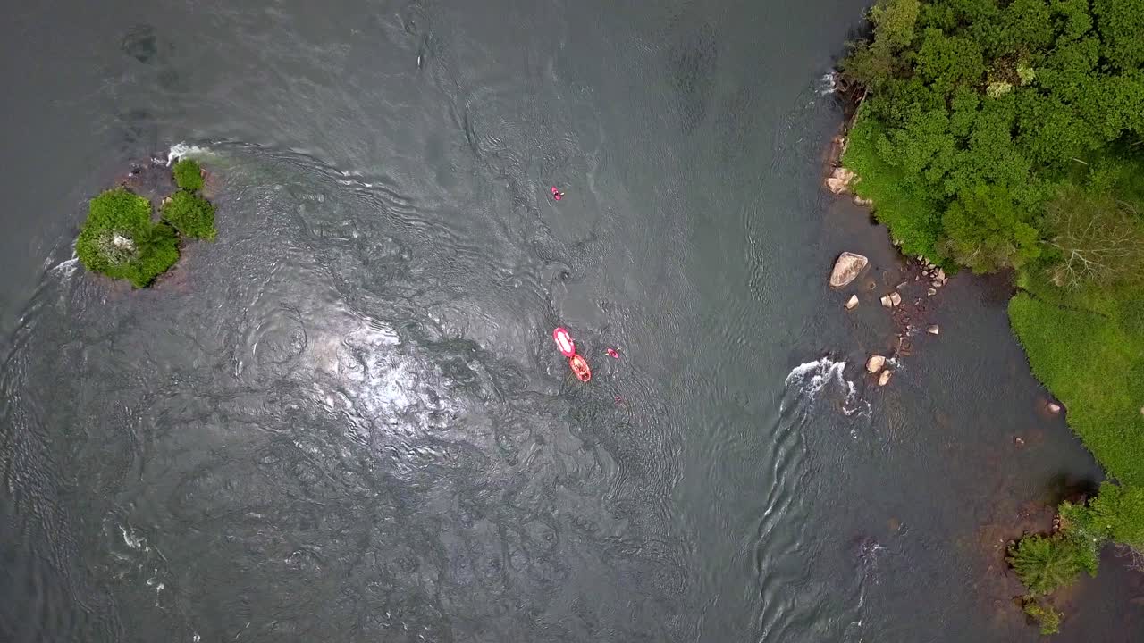 Top-down slow motion aerial of white water rafting on the Nile River near Jinja, Uganda. Rafters navigate Grade V rapids amid swirling currents, spray, and lush tropical riverbanks
