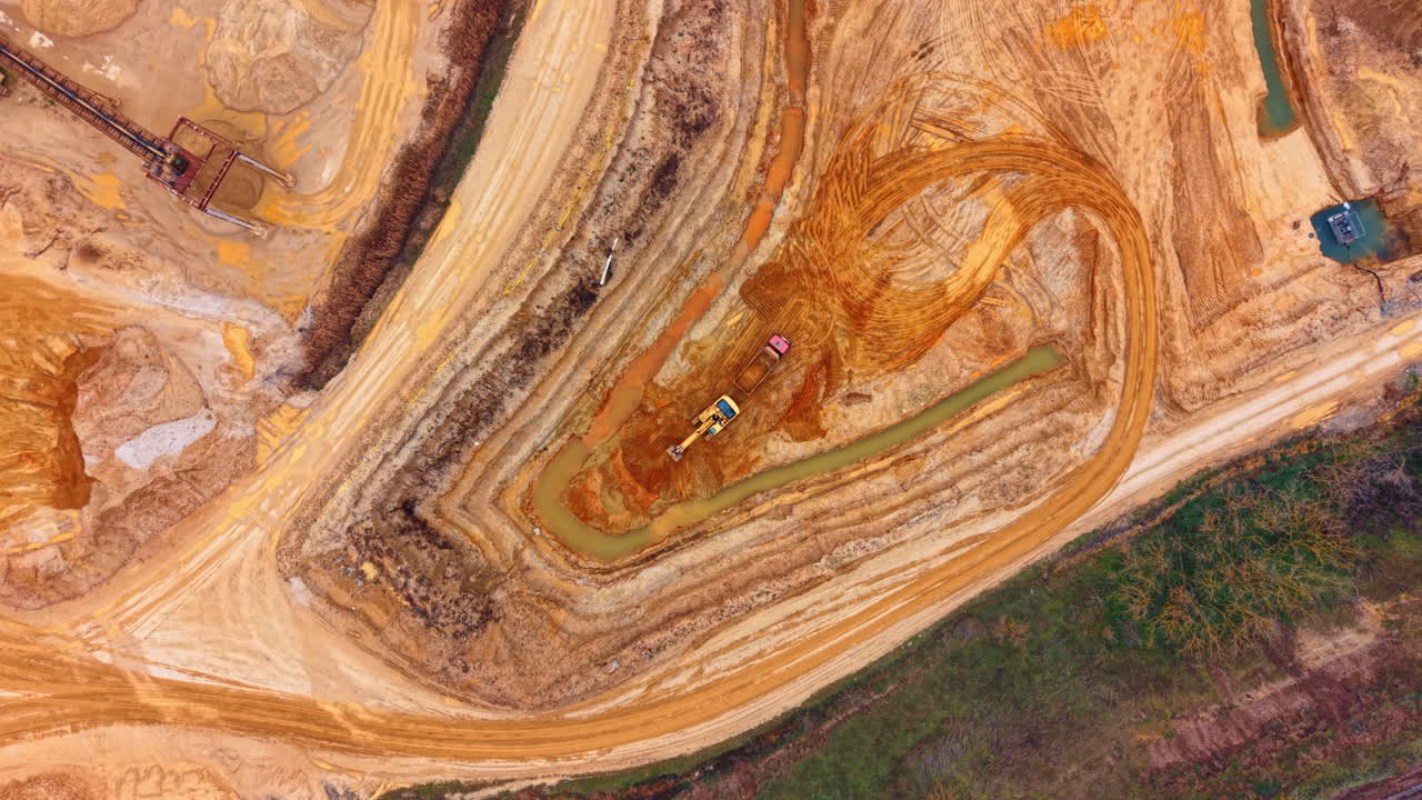 Top down aerial view of heavy machinery in quarry. Vertical drone shot of excavator and truck in sand pit