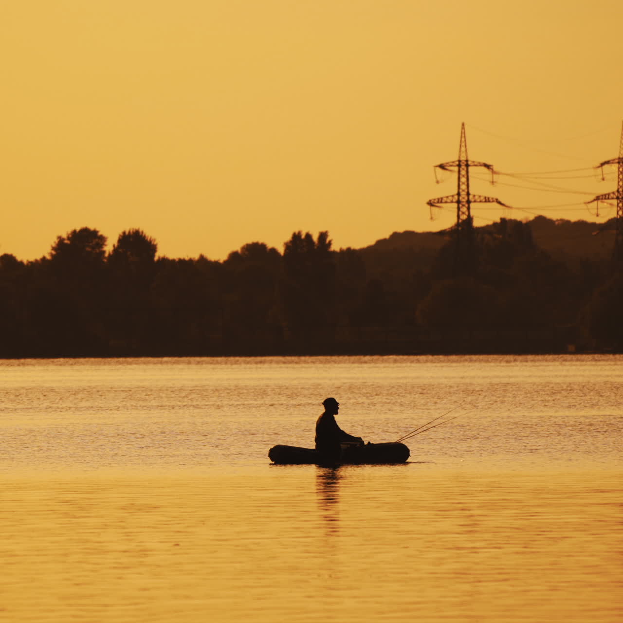 Silhouette of a man floating in a boat on the river surface on the background of an evening trees. Fisherman roams with oars while sailing on a row boat in the lake at beautiful sunset.