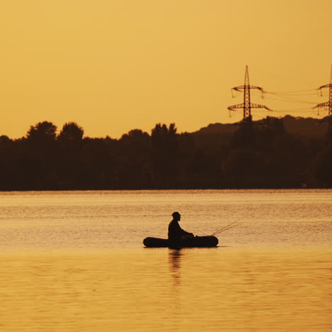 silhouette of a man floating in a boat on the river surface on the background of an evening trees. fisherman roams with oars while sailing on a row boat in the lake at beautiful sunset.