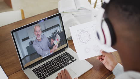 hombre de negocios afroamericano sentado en un escritorio usando una computadora portátil haciendo una videollamada con un colega masculino