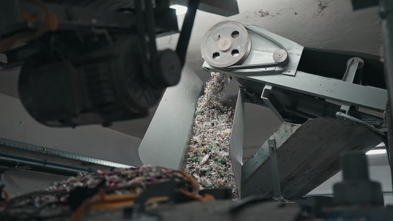 goma triturada cayendo por una rampa de metal en una planta de reciclaje industrial