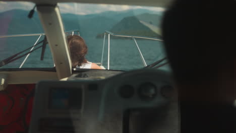 woman tourist sails contemporary yacht with skipper silhouette in exotic lagoon. passenger rests on deck while professional yachtsman drives motorboat