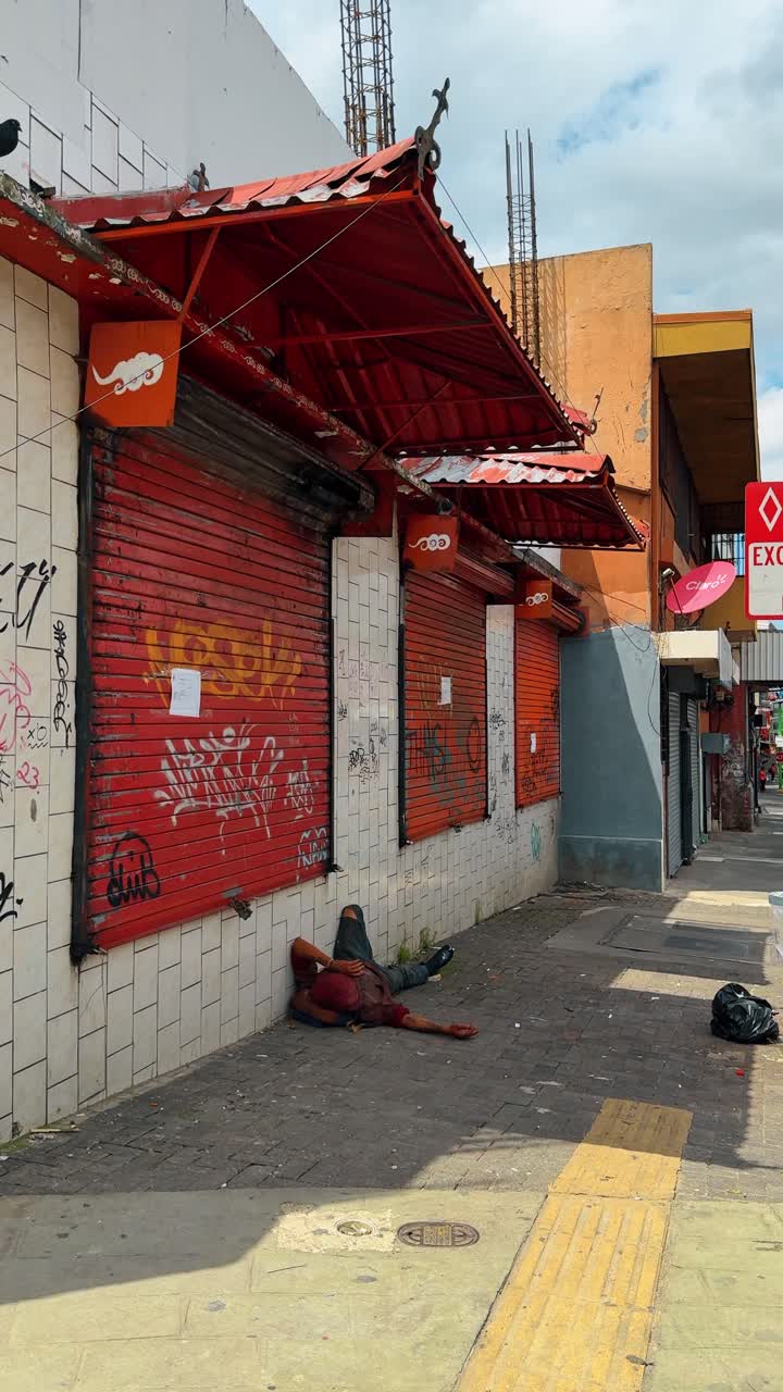 San José, Costa Rica, 7 de agosto de 2025: Persianas vermelhas de loja com grafite na rua de San José. Loja urbana fechada com persianas metálicas vermelhas e arte de rua, homem deitado na calçada na Costa Rica