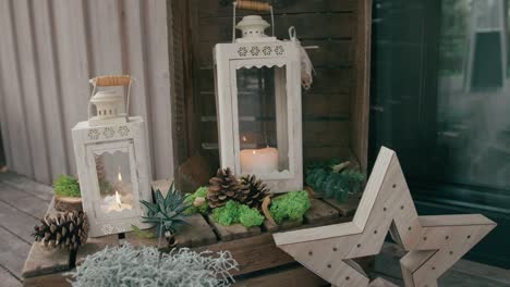 Decoraciones-Hechas-Con-Velas-Dentro-De-Farolillos-Blancos,-Pequeñas-Plantas-Y-Piñas,-Sobre-Una-Superficie-De-Madera