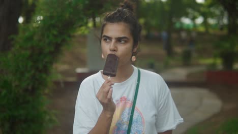 Una-Joven-Adolescente-Comiendo-Helado-De-Barra-De-Chocolate-En-El-Parque:-El-Concepto-De-Vacaciones,-Despreocupación-Y-Relajación