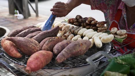 close up of female hand turning sweet potatoes while baking above hot embers