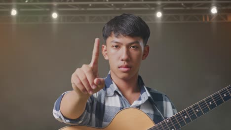 primer plano de un adolescente asiático con una guitarra sin mostrar ningún gesto mientras está de pie en el escenario