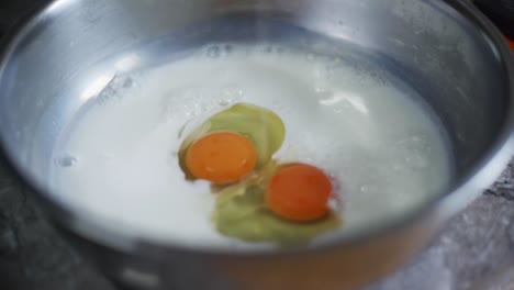 freshly cracked egg yolk dropped into bowl of milk, filmed as closeup slow motion shot