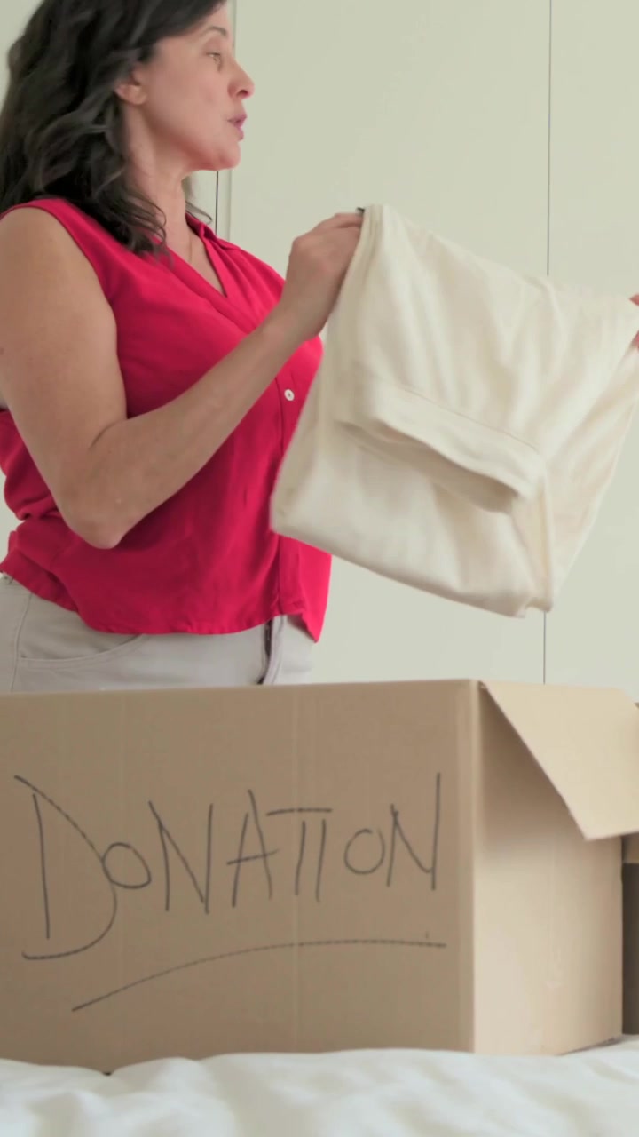 Vertical video: Opening DONATION box, couple in red top folding and packing items at home to donate