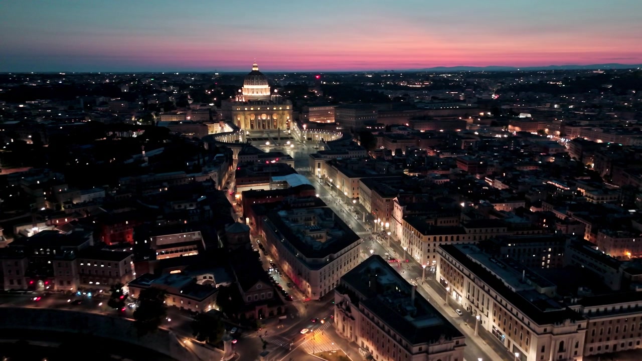 Le luci della città di Roma conducono verso Piazza San Pietro e la cupola luminosa del Vaticano mentre un drone sorvola lo skyline serale