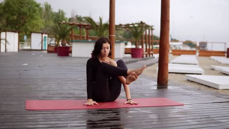 Mädchen-In-Schwarz-Macht-Yoga-Auf-Holzboden-Am-Strand,-Das-Mädchen-Führt-Yoga-Elemente-Durch,-Die-Das-Körpergewicht-Auf-Den-Händen-Ausgleichen