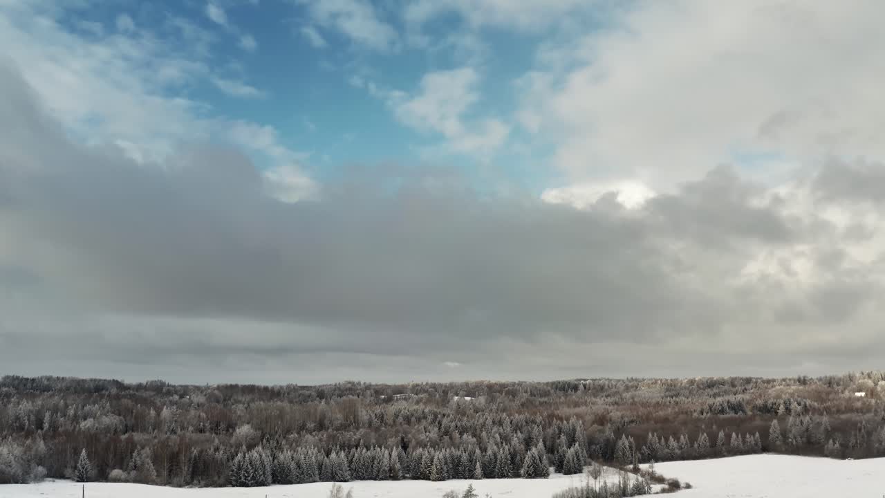 Stunning aerial drone view of snowy winter forest under a dramatic cloudy sky with sunlight breaking through.
